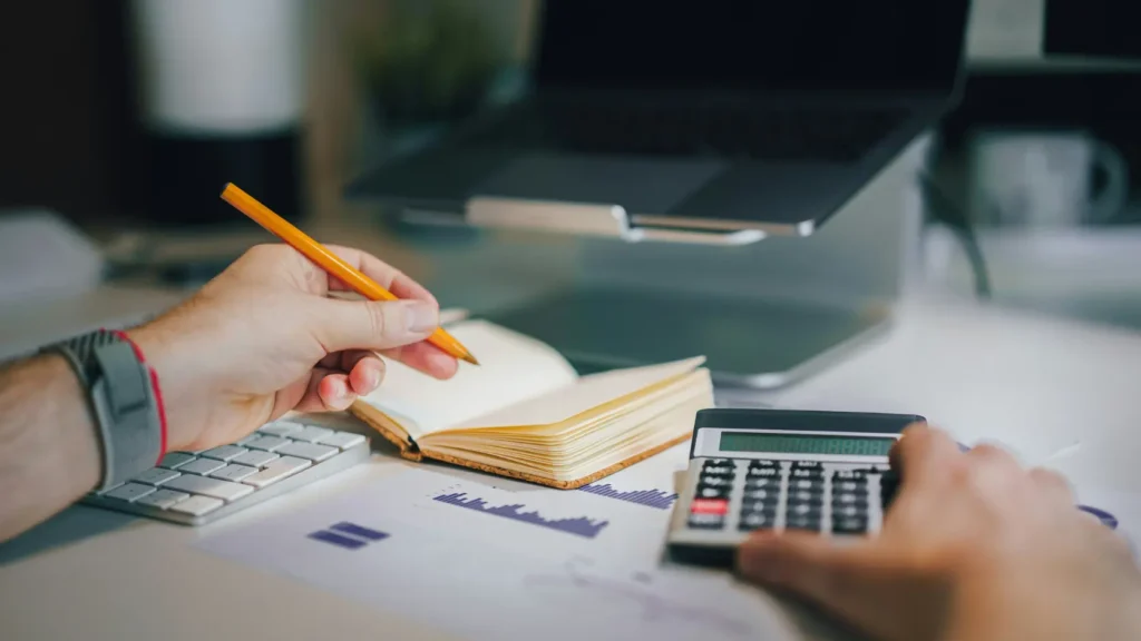 Calculadora y documentos financieros junto a portátil sobre mesa, representando el análisis de costes entre comprar, financiar o alquilar placas solares