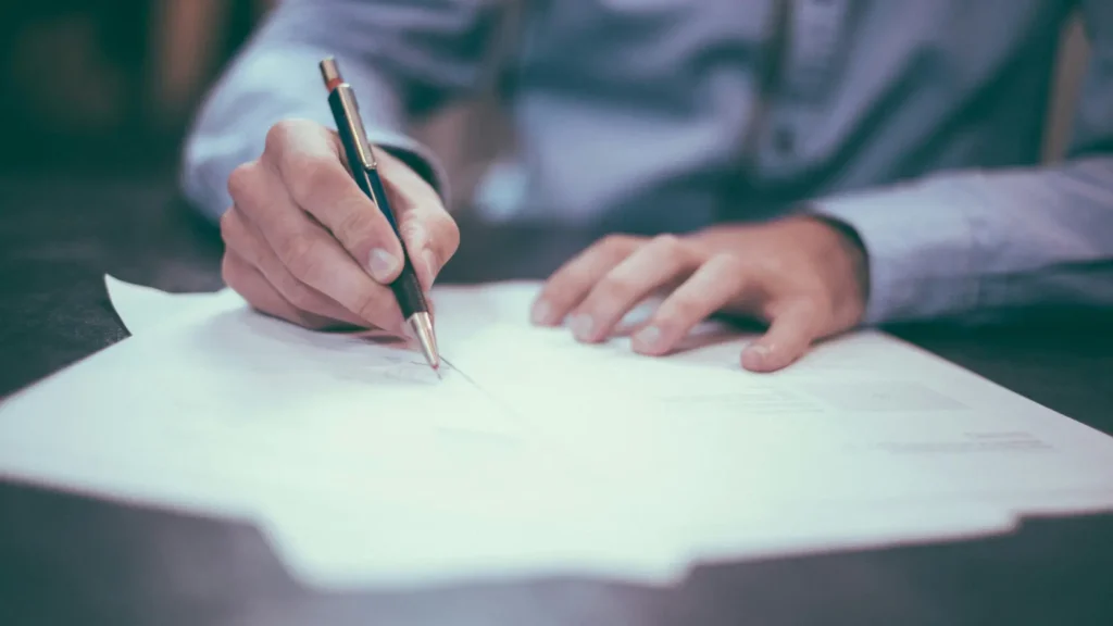 Primer plano de mano firmando un contrato sobre mesa con documentos, representando el momento de firmar un contrato de renting fotovoltaico